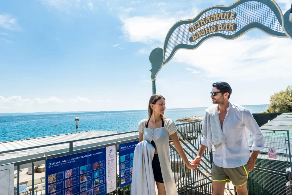 Coppia che si tiene per mano vicino all'ingresso del Miramare Bagno Bar con vista sul mare.